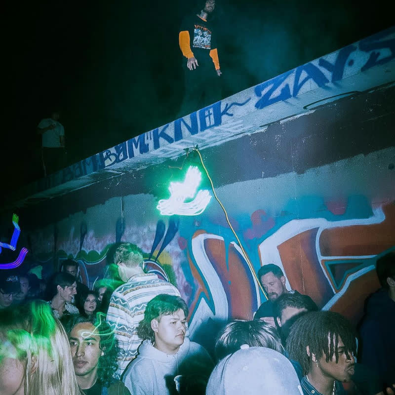 Crowd under graffiti at a previous No Expectations warehouse rave, lit in green